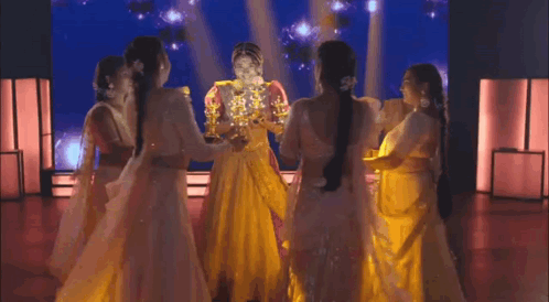 A Group Of Women In White Dresses Are Dancing On A Stage In Front Of A Large Screen . GIF