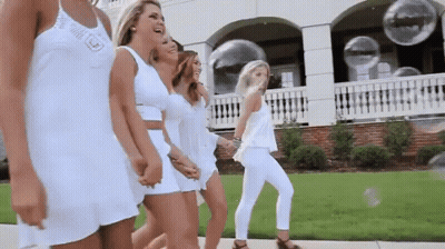 A Group Of Women In White Dresses Are Walking Down The Street . GIF
