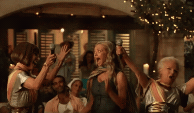 A Group Of Women Singing Into Microphones In A Crowd GIF