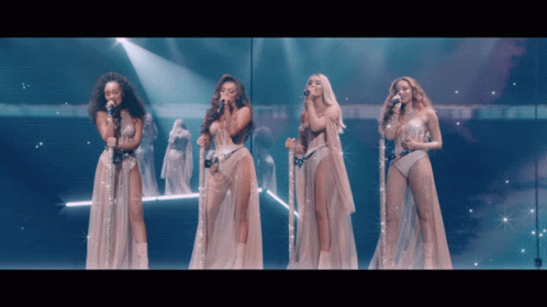 A Group Of Women Singing Into Microphones On A Stage With Angels In The Background GIF