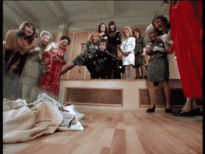 A Group Of Women Standing Around A Man In A Room GIF