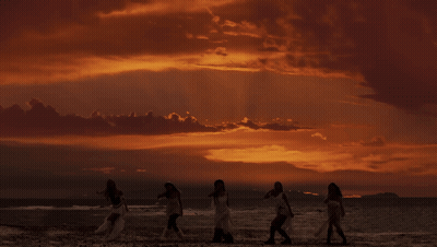A Group Of Women Standing On A Beach At Sunset GIF
