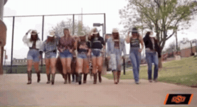 A Group Of Women Wearing Cowboy Hats And Shorts Walking Down A Sidewalk GIF