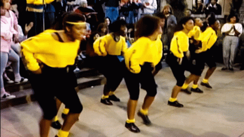 A Group Of Women Wearing Yellow Shirts And Black Pants Are Dancing In Front Of A Crowd GIF
