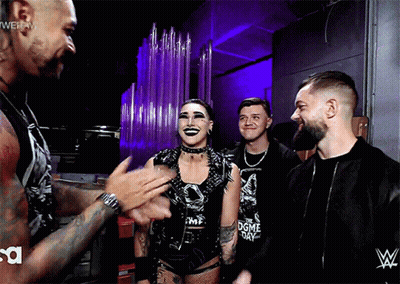 A Group Of Wrestlers Are Standing In A Room With A Wwe Logo On The Wall GIF