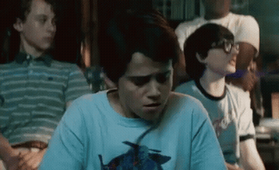 A Group Of Young Boys Are Sitting In A Room And One Of Them Is Wearing A Blue Shirt With A Bird On It . GIF