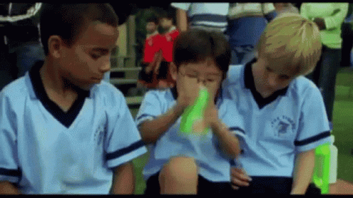 A Group Of Young Boys Wearing Blue Jerseys Are Sitting On A Soccer Field . GIF