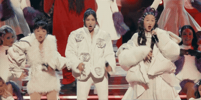 A Group Of Young Girls In White Dresses And Fur Coats Are Dancing On A Stage GIF