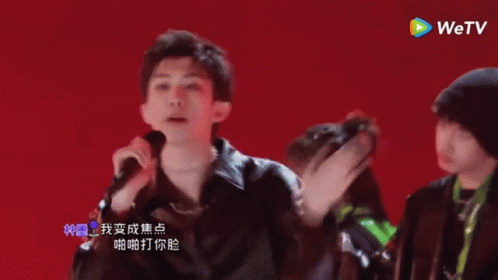 A Group Of Young Men Are Dancing And Singing In Front Of A Red Background With A Wetv Logo In The Corner GIF