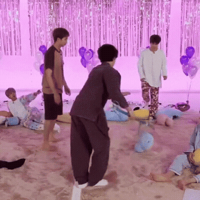 A Group Of Young Men Are Playing A Game In A Room With Balloons And A Purple Curtain . GIF