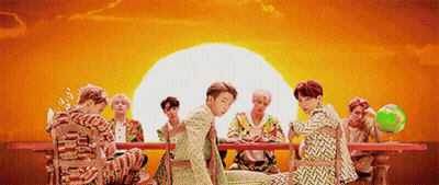 A Group Of Young Men Are Sitting Around A Table With A Globe In Front Of A Sunset . GIF