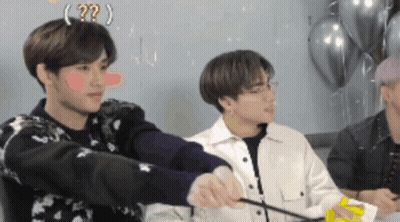 A Group Of Young Men Are Sitting Around A Table With Balloons In The Background And One Of Them Has A Question Mark On H GIF