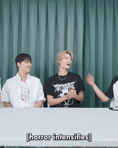 A Group Of Young Men Are Sitting At A Table And One Of Them Is Wearing A Black Shirt That Says " Horror Intensifies " GIF