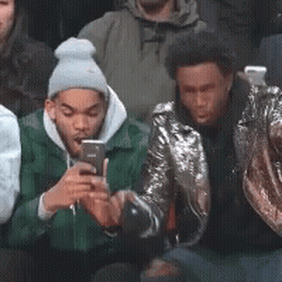 A Group Of Young Men Are Sitting In A Crowd Looking At Their Cell Phones . GIF