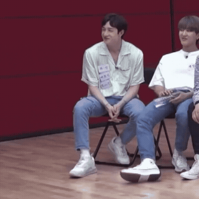 A Group Of Young Men Are Sitting In Chairs On A Wooden Floor In Front Of A Red Wall . GIF