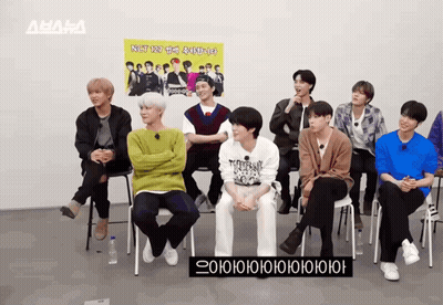 A Group Of Young Men Are Sitting In Front Of A Sign That Says Nst GIF