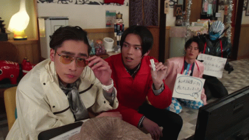 A Group Of Young Men Are Sitting In Front Of A Television And One Of Them Is Holding A Sign That Says ' A ' GIF