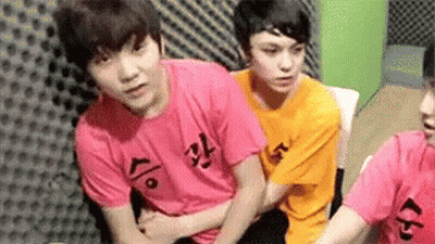 A Group Of Young Men Are Sitting Next To Each Other In A Room Wearing Pink And Orange Shirts . GIF