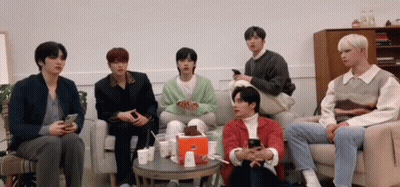 A Group Of Young Men Are Sitting On A Couch Looking At Their Cell Phones . GIF