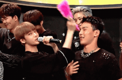 A Group Of Young Men Are Standing Around A Man Holding A Microphone And A Fan GIF