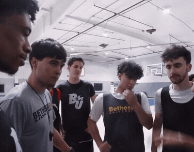 A Group Of Young Men Are Standing In A Gym And One Of Them Is Wearing A Shirt That Says Bethess University GIF
