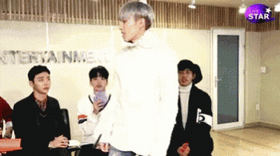 A Group Of Young Men Are Standing In A Room With The Word Entertainment On The Wall Behind Them GIF