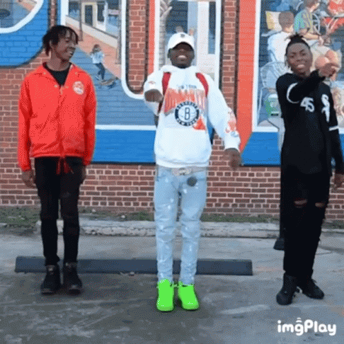 A Group Of Young Men Are Standing In Front Of A Brick Building . GIF
