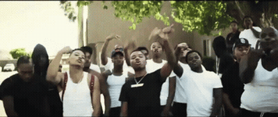 A Group Of Young Men Are Standing In Front Of A Building With Their Hands In The Air . GIF