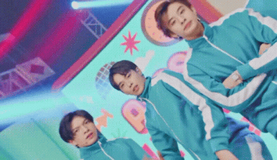 A Group Of Young Men Are Standing Next To Each Other On A Stage In Squid Game Costumes . GIF