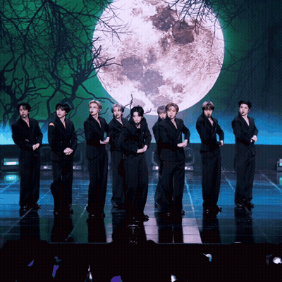 A Group Of Young Men Are Standing On A Stage In Front Of A Full Moon GIF