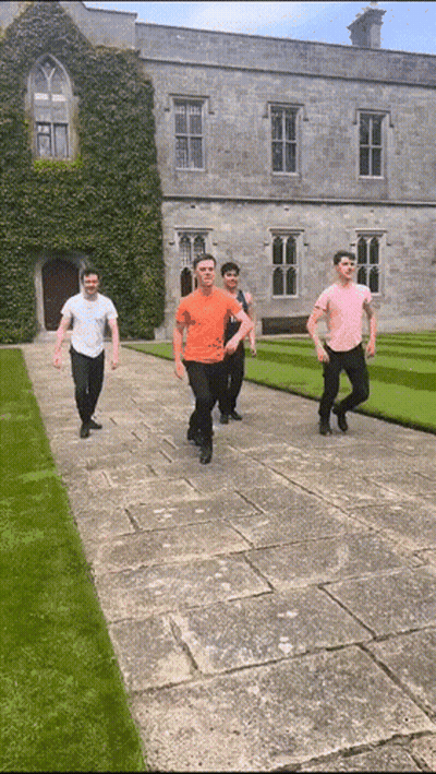 A Group Of Young Men Are Walking Down A Stone Walkway In Front Of A Large Building GIF