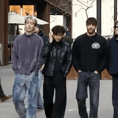 A Group Of Young Men Are Walking Down A Street And One Of Them Is Wearing Headphones GIF