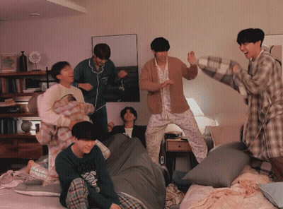 A Group Of Young Men In Pajamas Are Having A Pillow Fight In A Room GIF