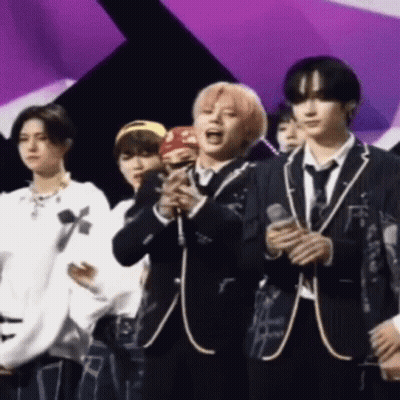 A Group Of Young Men In Suits And Ties Are Standing On A Stage Holding Microphones . GIF