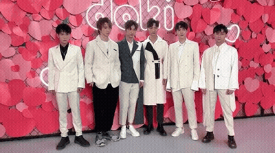 A Group Of Young Men In Suits Are Standing In Front Of A Wall Made Of Hearts . GIF