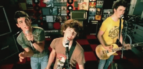 A Group Of Young Men Singing And Playing Guitars In Front Of A Wall That Says Try On It GIF
