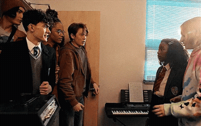 A Group Of Young People Are Standing Next To Each Other In A Room With A Piano . GIF