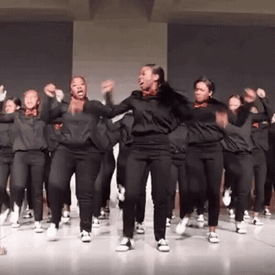 A Group Of Young Women Are Dancing Together On A Stage In A Room . GIF