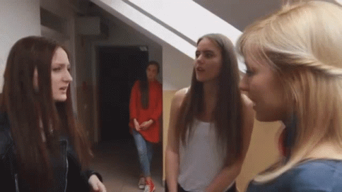 A Group Of Young Women Are Standing In A Hallway Talking To Each Other . GIF