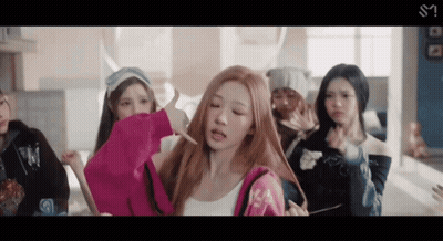 A Group Of Young Women Are Standing In A Room And One Of Them Is Holding A Pink Hoodie GIF