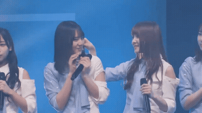 A Group Of Young Women Are Standing In Front Of A Blue Background And One Of Them Is Holding A Microphone GIF