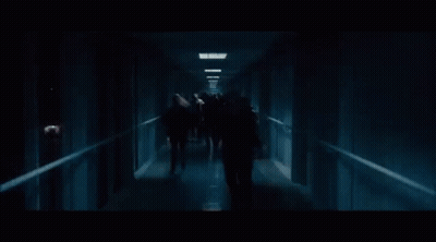 A Group Of Zombies Are Walking Down A Hallway . GIF