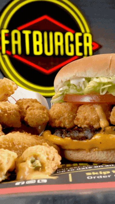 A Hamburger And Fried Shrimp Are On A Plate In Front Of A Sign That Says Fatburger GIF