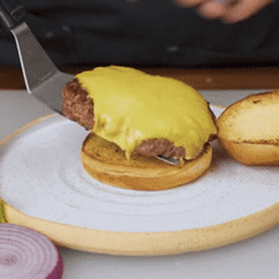A Hamburger Is Being Served On A White Plate With A Spatula GIF