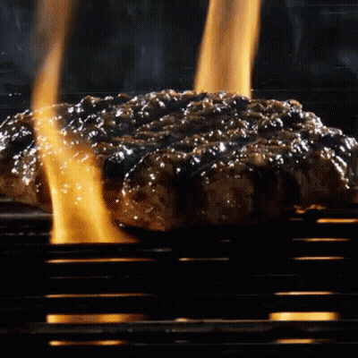 A Hamburger Is Cooking On A Grill With Flames Behind It GIF