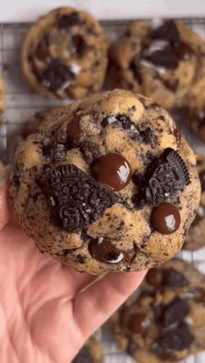 A Hand Is Holding A Cookie With Oreos And Chocolate Chips On It . GIF