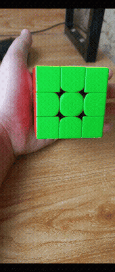 A Hand Is Holding A Green And Red Cube On A Wooden Table GIF
