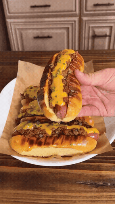 A Hand Is Holding A Hot Dog On A Plate GIF