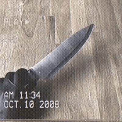 A Hand Is Holding A Knife On A Wooden Surface . GIF