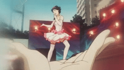 A Hand Is Holding A Picture Of A Girl In A Tutu Singing Into A Microphone . GIF